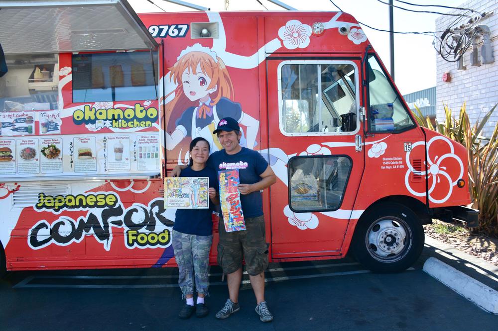 Chizuru and Gerald Abraham stand in front of Okamoto Kitchen holding the truck's menu